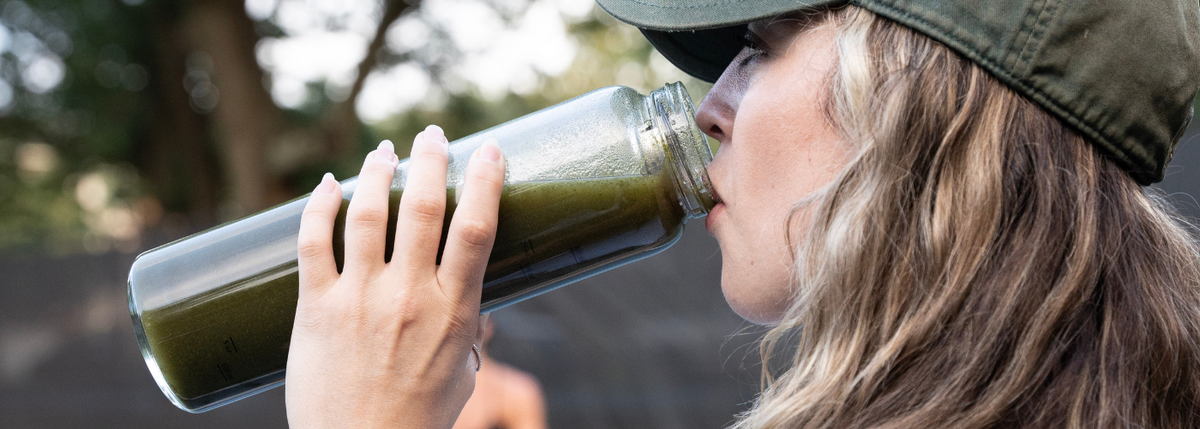 Woman drinking green juice out of a clear water bottle