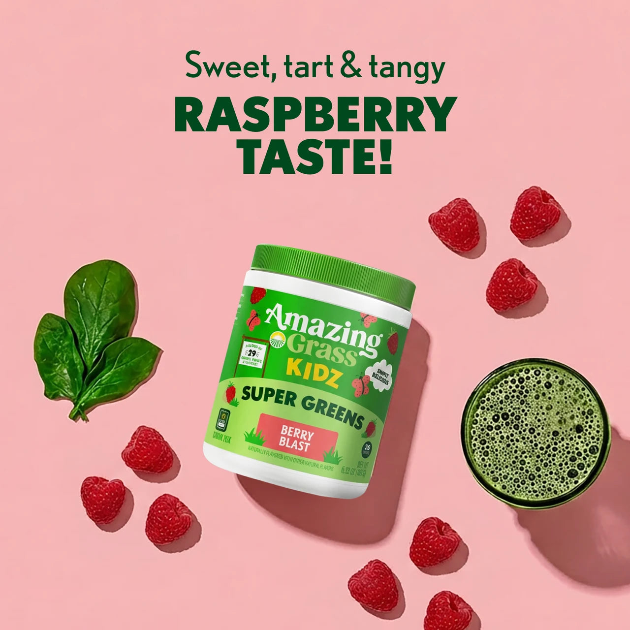 Container of Amazing Grass Kidz Super Greens with raspberries and a green smoothie on a pink background