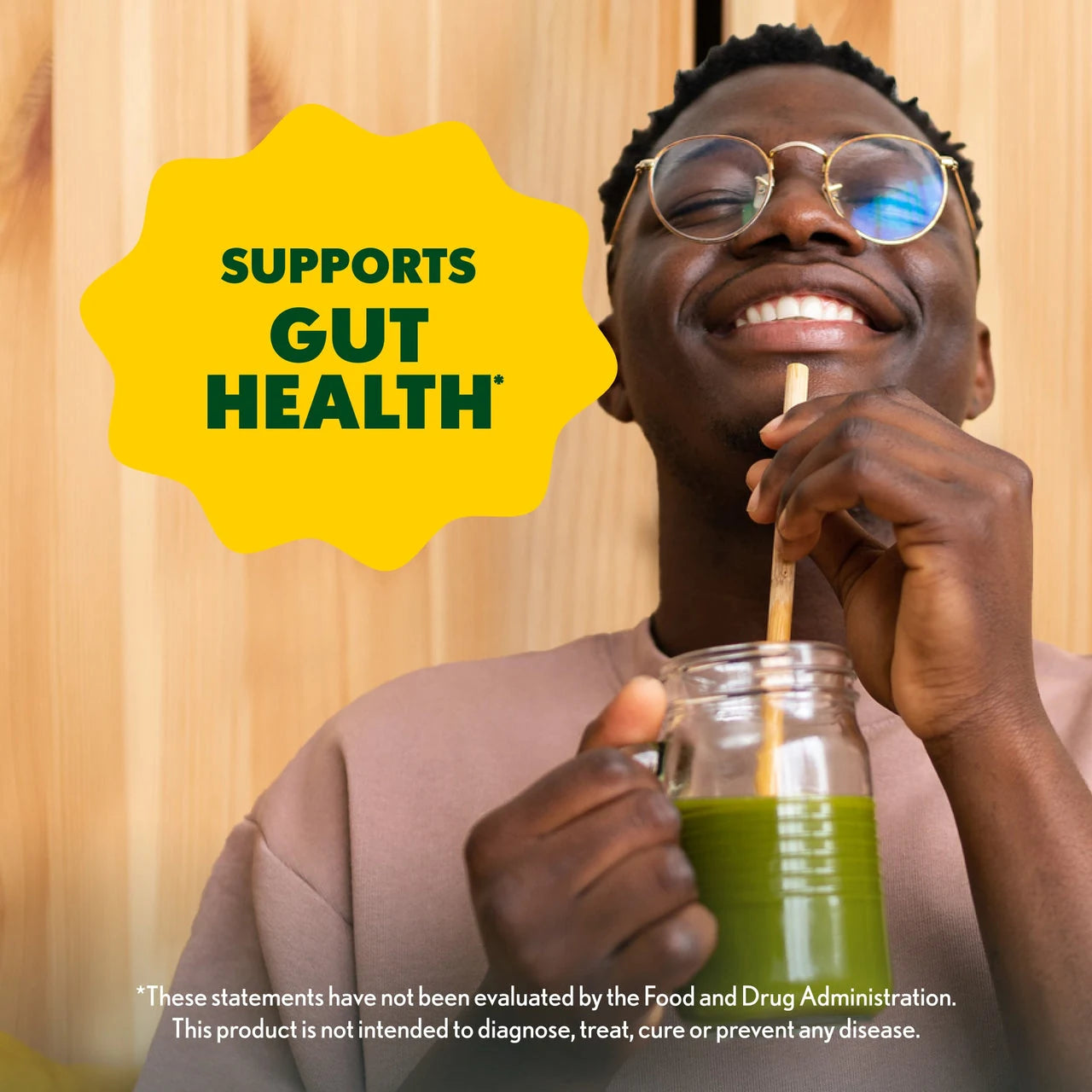 Person drinking green juice with a straw, wearing glasses, against a wooden background with 'Supports Gut Health' text.
